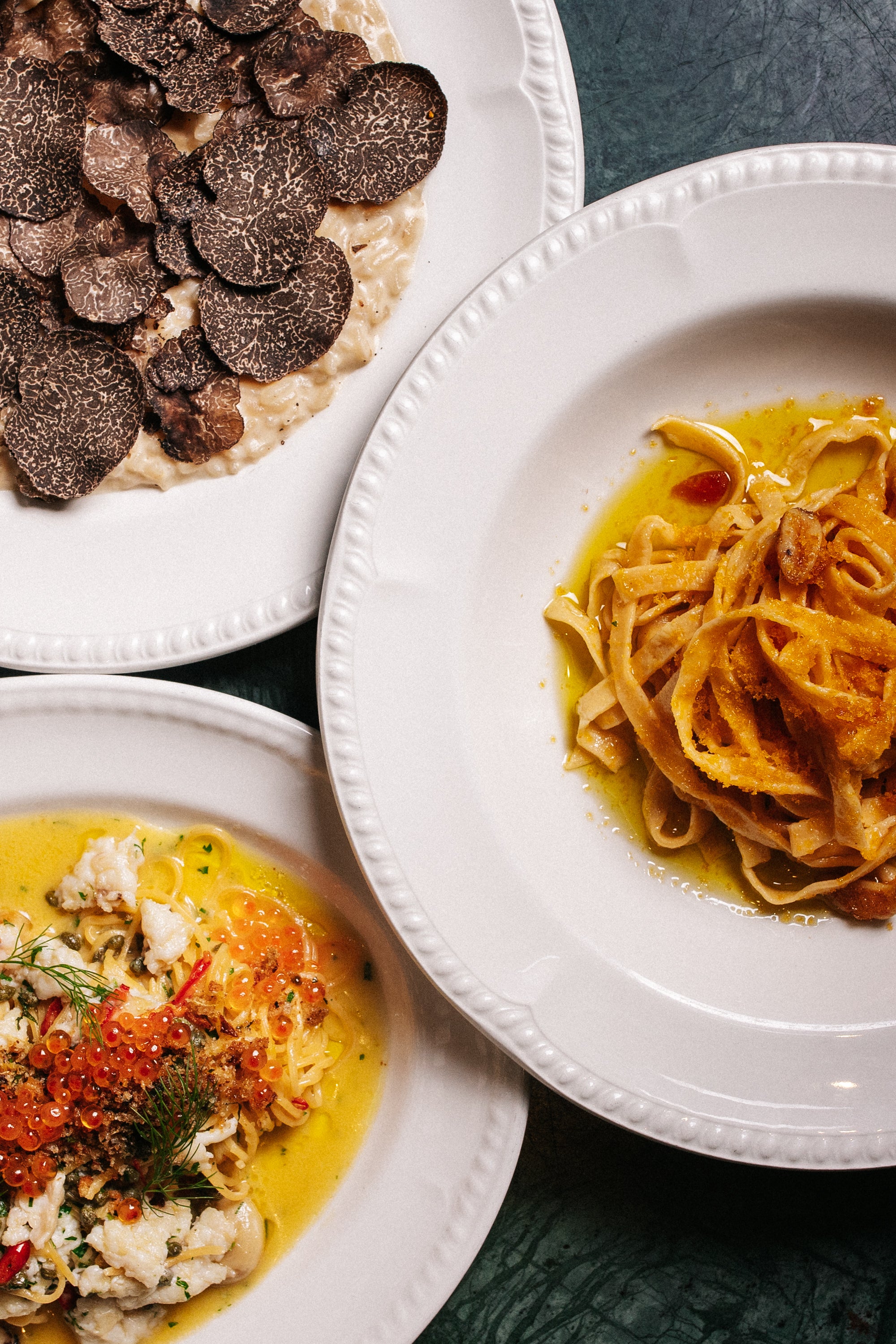 Three plates of pasta with different City Cellar dishes on a dark surface