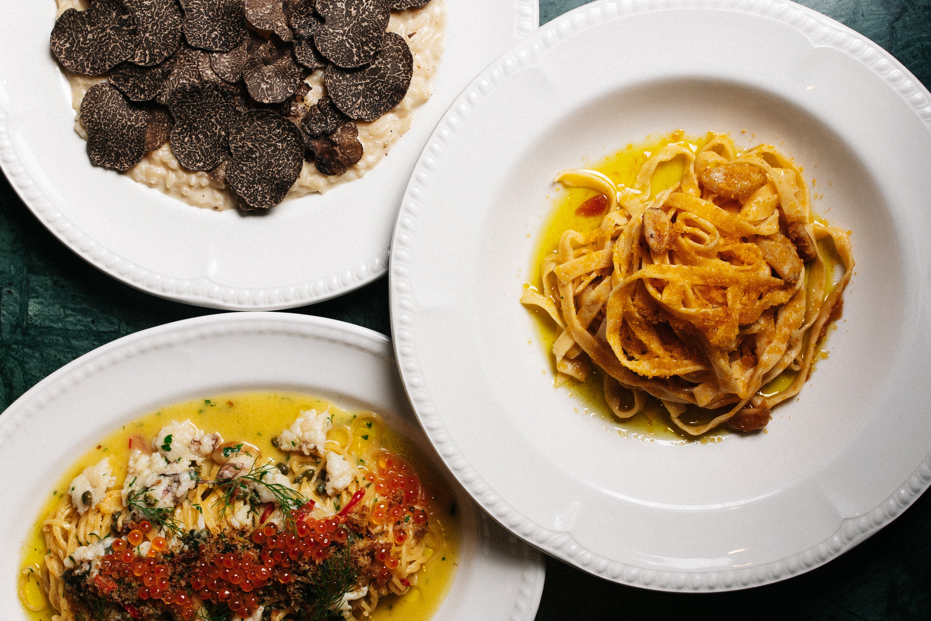 Three plates of pasta with different City Cellar dishes on a dark surface