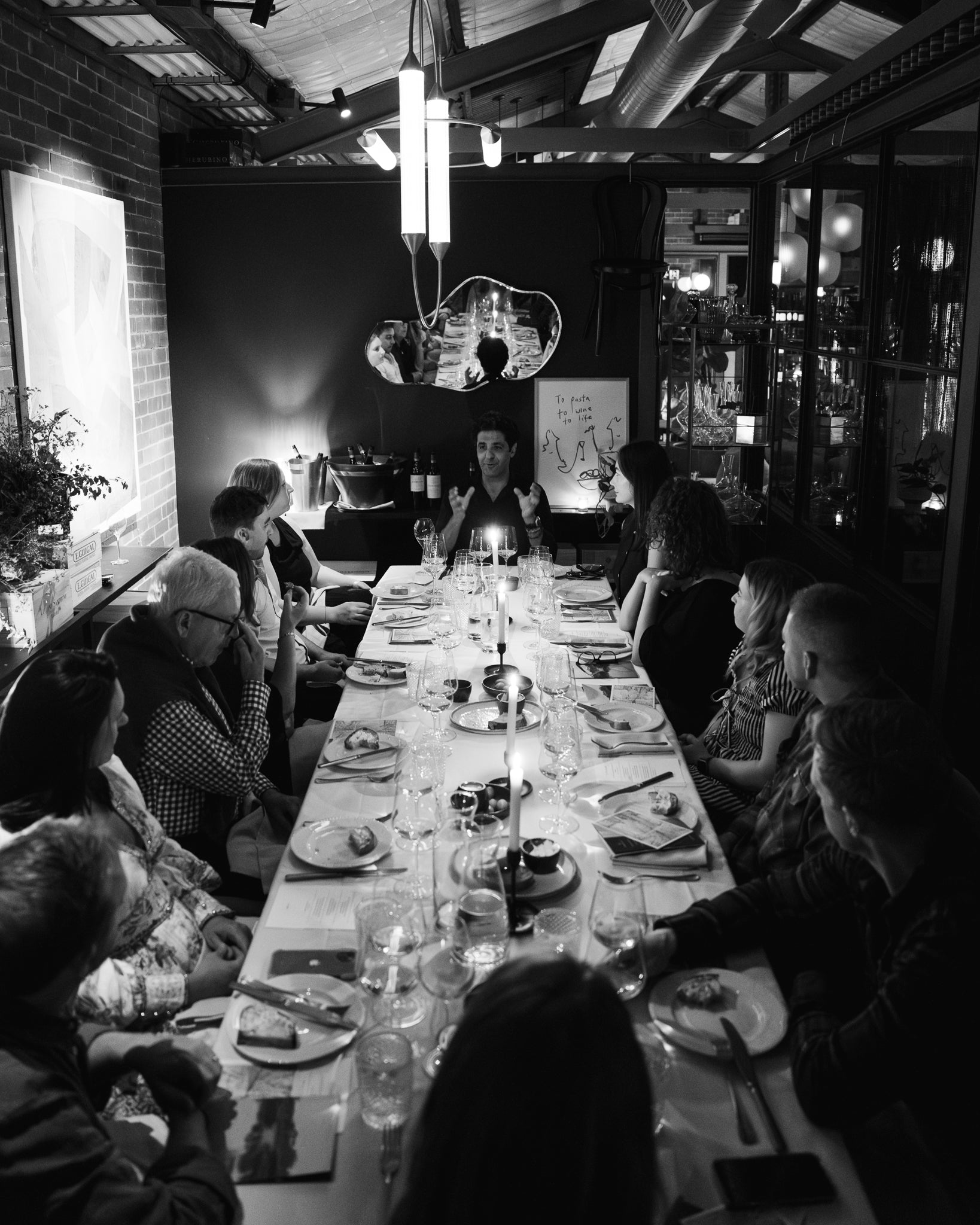 Dinner party with guests seated around a long table in a dimly lit room.