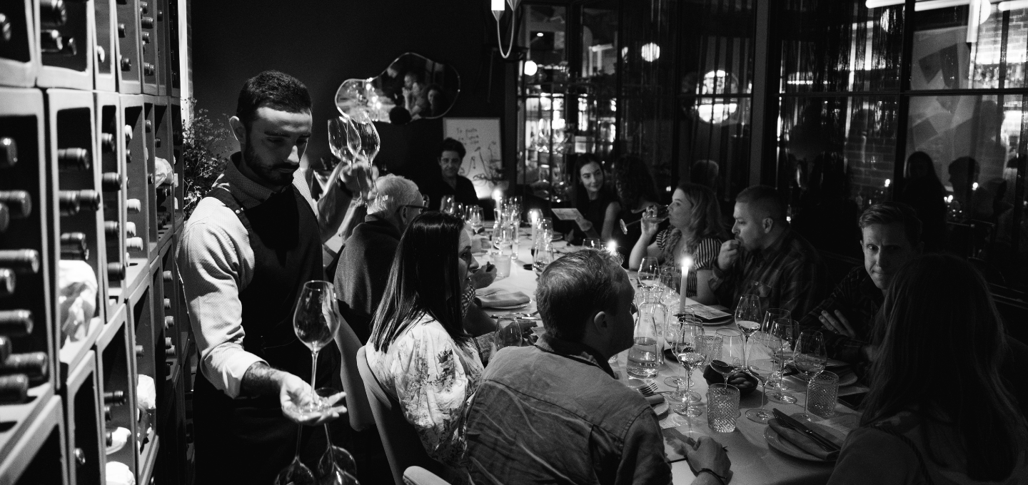 Dinner party with guests seated at a table in a dimly lit room.