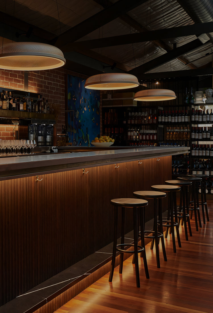 Bar area with wooden counter, stools, and shelves with bottles in a dimly lit setting.
