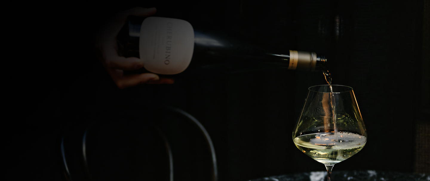 White wine being poured from a bottle into a glass against a dark background
