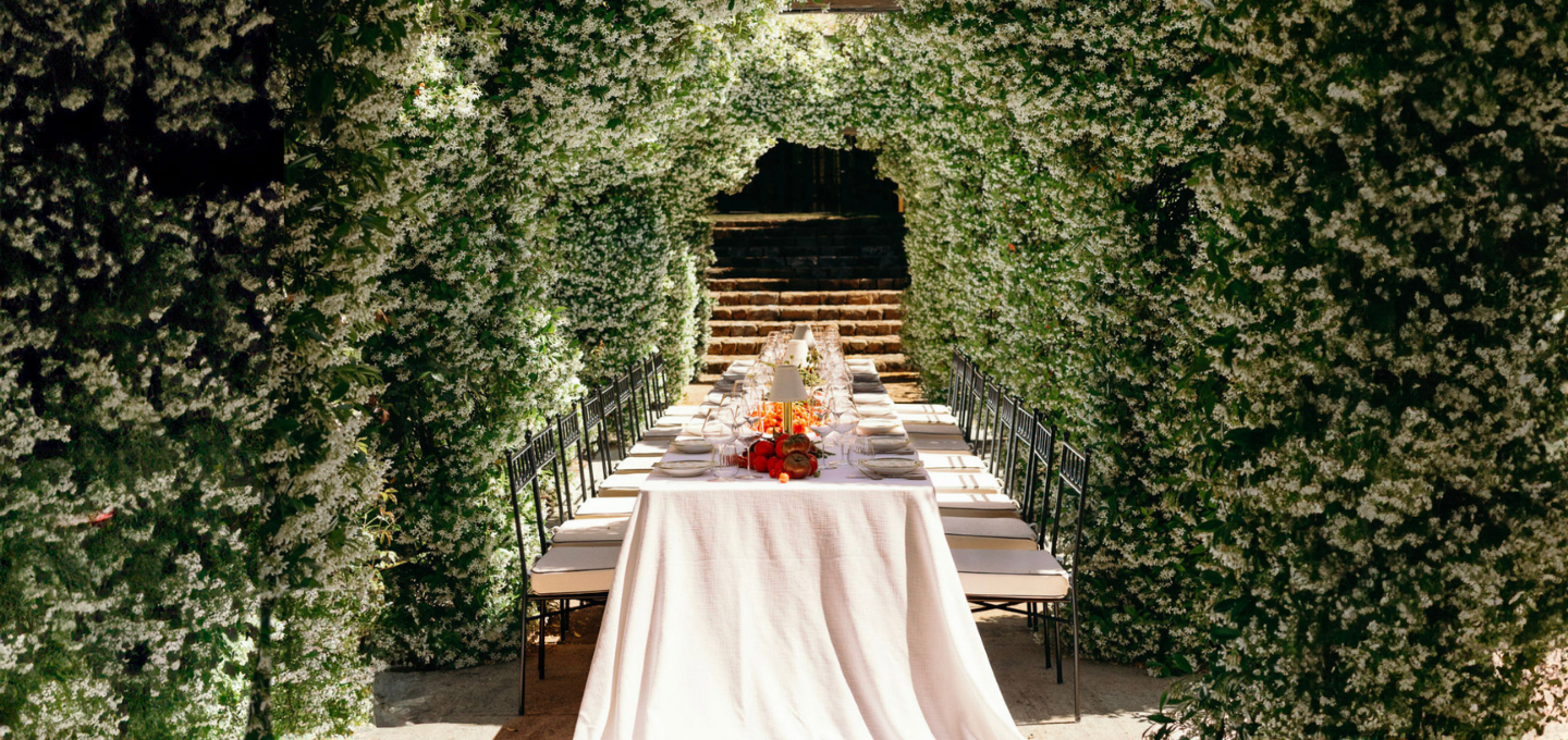 Long dining table set for a meal under a canopy of greenery