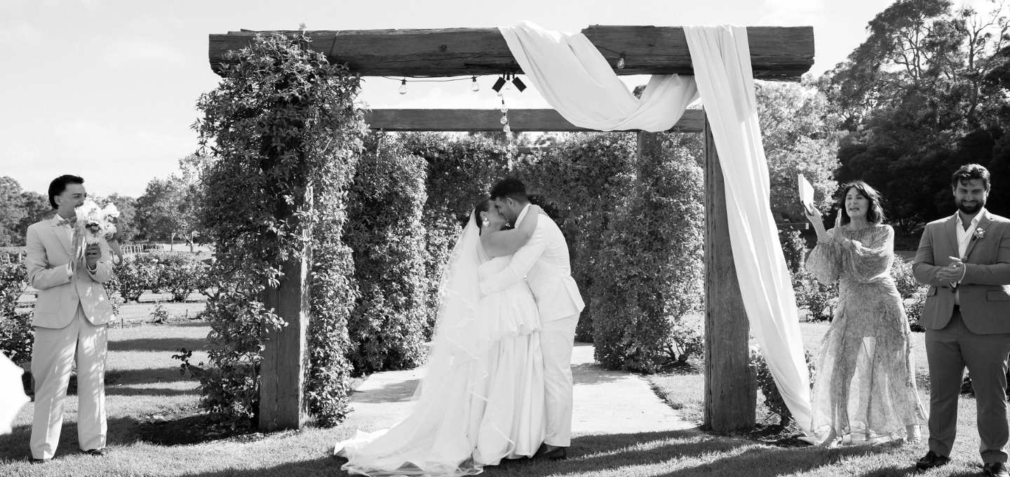 Wedding ceremony with a couple under an archway in a garden setting.