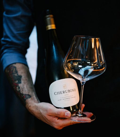 Person holding a bottle and a glass of Cherubino wine against a dark background