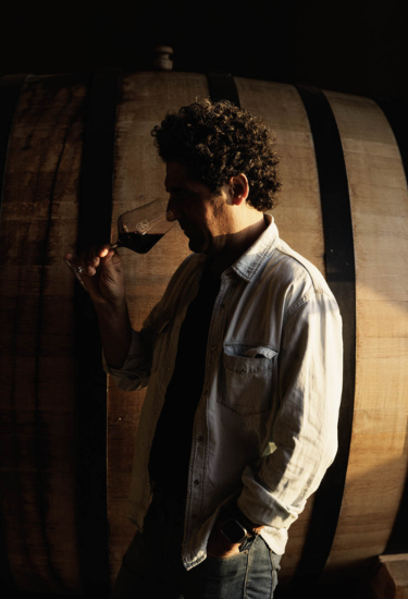 Larry Cherubino, winemaker holding a glass of wine in front of a barrel