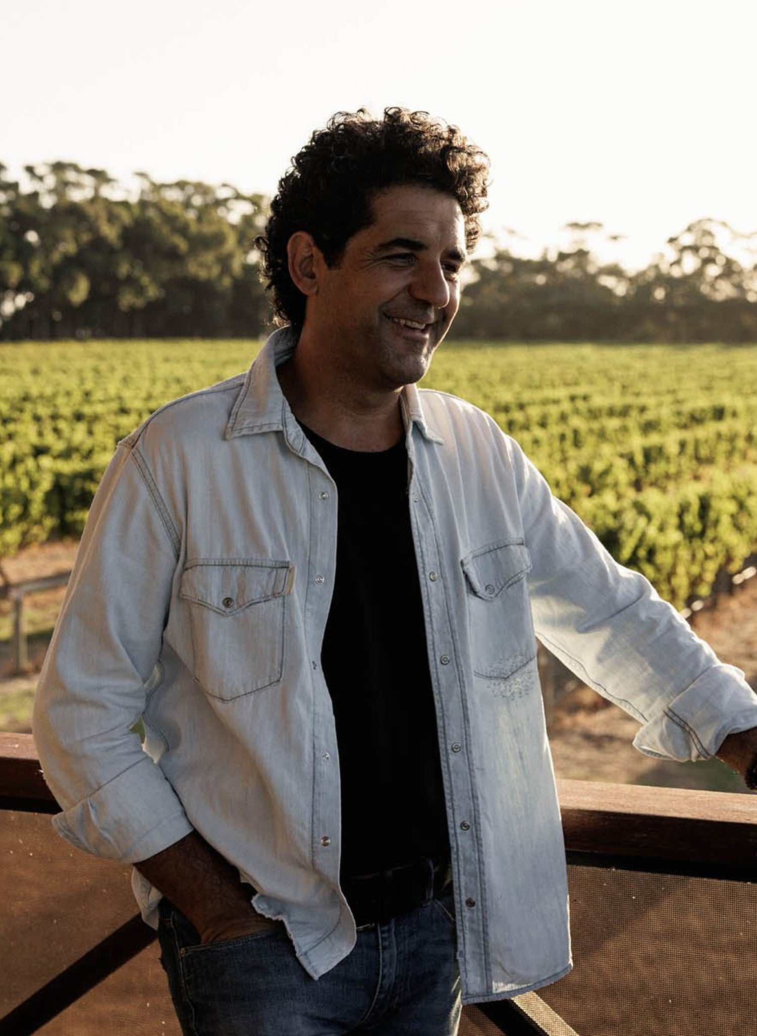 Man standing in a vineyard wearing a light jacket and dark shirt.