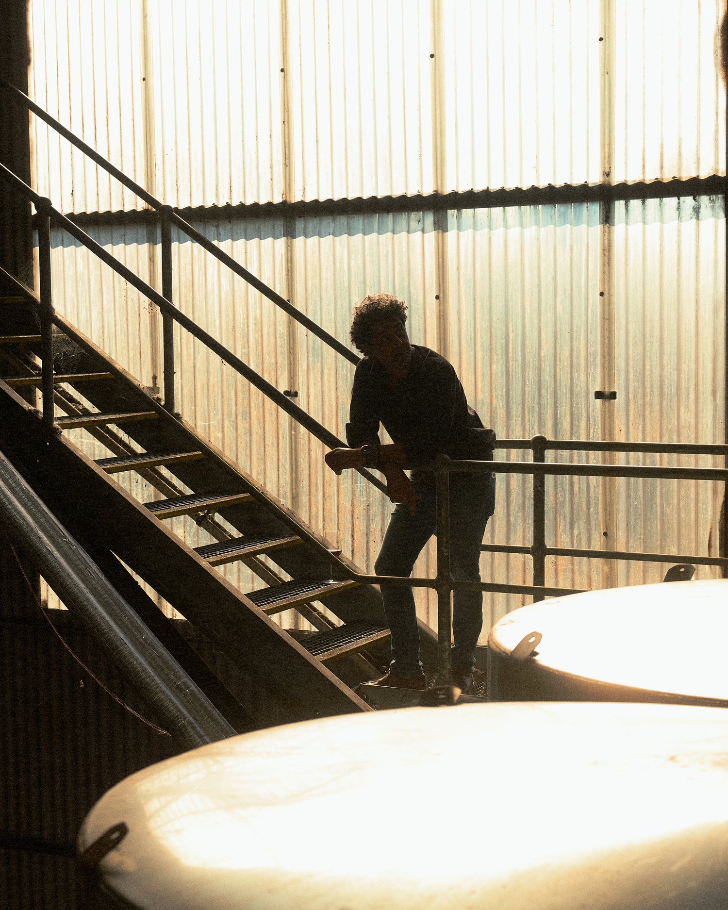 Larry Cherubino standing on a staircase in Cherubino Wines winery with sunlight filtering through.